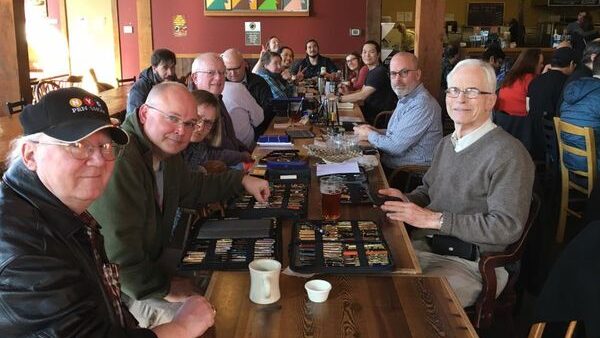 A group of people sitting at a long table, with open cases of fountain pens displayed on the table in front of them.