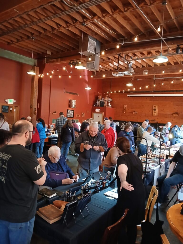A crowd of people inspecting pens on a table